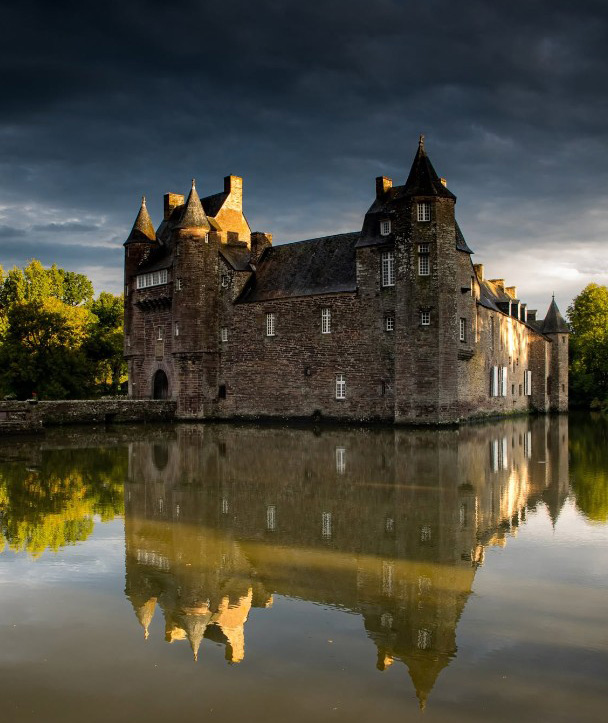Le château de Trécesson en schiste rouge se reflétant dans les eaux de son étang, aux portes de Brocéliande