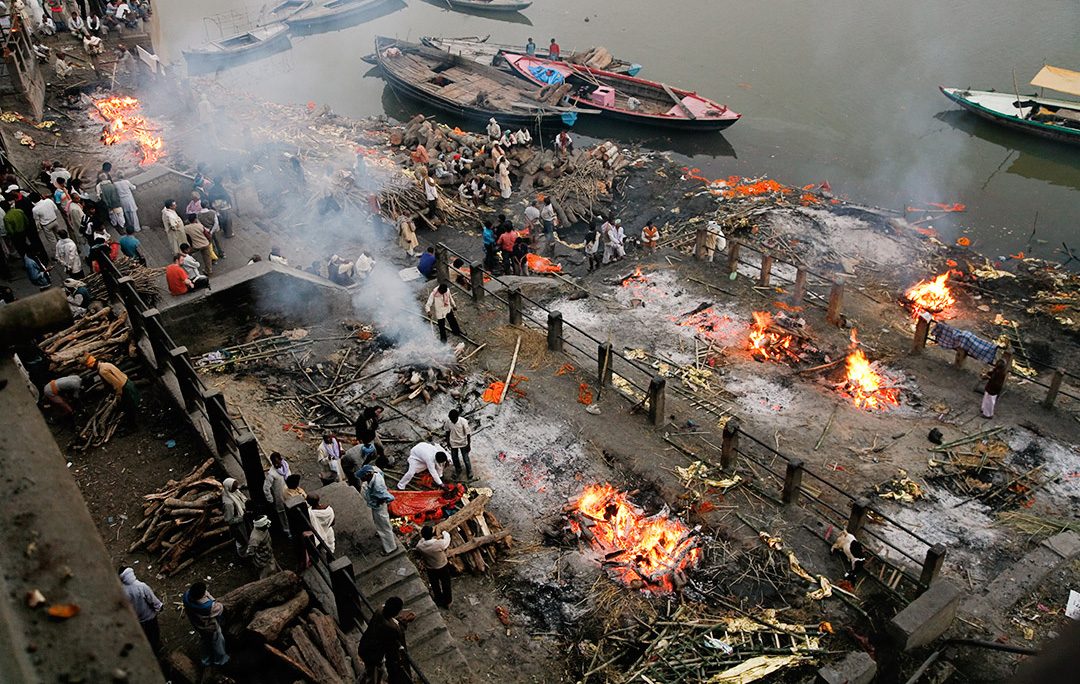 Les ghâts de Varanasi au bord du Gange à l'aube, avec les fumées des feux de crémation qui s'élèvent dans la brume